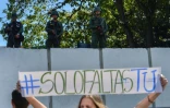 Une femme brandit une pancarte "#Il ne manque que toi" devant des soldats surveillant un quartier général de l'armée, à Caracas le 27 janvier 2019 
