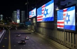 Des voitures passent le 4 mars 2026 devant des écrans géants installés le long de l'autoroute à Tel Aviv, affichant les drapeaux des Etats-Unis et d'Israël