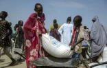 Un garçon et sa mère soulèvent un sac de maïs pour le charger dans leur brouette, dans un centre de distribution du camp de déplacés à Bentiu, dans l'État d'Unity, au Soudan du Sud, le 6 novembre 2025