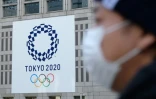 Un passant portant un masque antivirus devant le logo des Jeux olympiques 2020 de Tokyo, le 19 mars 2020 à Tokyo