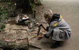 Tamara Nesterenko prépare un feu pour la cuisine de fortume installée à l'extérieur d'un abri à Severodonetsk, le 18 mai 2022 en Ukraine