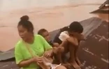 Sur cette capture d'écran d'une vidéo de ABC Laos le 24 juillet 2018, une femme et des enfants se sont réfugiés sur un toit entouré par les eaux déversées par la rupture du barrage de Xe-Pian-Xe.