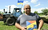 L'agriculteur Viktor Kytchouk montre le dessin d'un timbre ukrainien représentant un tracteur remorquant un char russe sous un ciel jaune, le 28 juillet 2022 dans un champ près de Mala Rogan, dans la région de Kharkiv