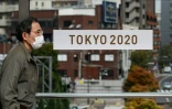 Un passant masqué devant une banderole pour les Jeux olympiques 2020 de Tokyo le 27 mars 2020 à Tokyo
