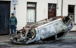 Un passant observe les restes d'une voiture calcinée, au lendemain d'une nouvelle nuit d'émeutes visant des immigrés, le 11 juin 2025 à Ballymena, en Irlande du Nord 