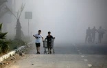 De la fumée lors d'une frappe israélienne alors que des Palestiniens marchent sur une route utilisée pour atteindre un point de distribution d'aide de la Fondation humanitaire de Gaza (GHF,) près du camp de réfugiés de Nousseirat, dans le centre de la bande de Gaza, le 25 juin 2025