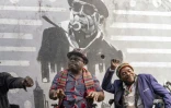 Coco Yakala (g) et Théophile Nzonga (d) dans leurs fauteuils roulants devant une affiche murale du fondateur de leur groupe de musique Ricky Likabu, posent dans les rues de Kinshasa, le 11 août 2021