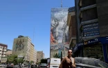 Une femme marche dans une rue près d'une immense fresque sur un immeuble faisant référence au "détroit d’Ormuz", dans la capitale Téhéran, le 9 mai 2026