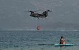 Un vacancier pratiquant le stand up paddle (planche à rame) observe un hélicoptère se ravitailler en eau près de la plage de Lambiri à Patras (Grèce) le 1er août 2021