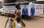 Une femme et ses enfants traversent la rue près d'un camion de campagne du président sortant du Cameroun, Paul Biya, à Yaoundé le 11 octobre 2025
