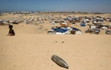 Un obus non explosé gît sur une dune de sable alors qu'un jeune garçon est assis près d'un camp de fortune pour les Palestiniens déplacés dans la zone de Tel al-Sultan à Rafah, dans le sud de la bande de Gaza, le 30 mai 2024