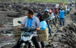 Des habitants roulent à moto sur un sentier de fortune fait de dalles de bois pour éviter la boue causée par des inondations dans le village de Rambatan, sur l'île indonésienne de Sumatra, le 14 mai 2024