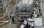 Des passagers d'un train marchent sur les rails après une interruption du trafic ferroviaire due à un fort séisme à Osaka au Japon, le 18 juin 2018