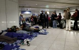 Des passagers dorment sur des matelas gonflables posés à même le sol tandis que d'autres font la queue à côté d'eux à l'aéroport international de Munich, dans le sud de l'Allemagne, tôt le matin du 4 octobre 2025