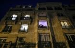 Des personnes se tiennent à leur fenêtre pendant les applaudissements quotidiens de 8 heures en soutien aux soignants, le 27 mars 2020 à Paris, au onzième jour d'un confinement visant à freiner la propagation du Covid-19 en France