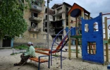 Une femme âgée se repose sur un banc dans une aire de jeu, devant des immeubles abîmés par des bombardements à Moshchun, près de Kiev en Ukraine, le 27 mai 2022