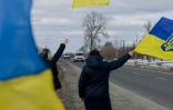 Des personnes agitent des drapeaux sur le bord  d'une route à l'approche d'un convoi de soldats libérés par les Russes après un échange de prisonniers, le 6 mars 2026 dans un lieu non précisé dans le nord de l'Ukraine