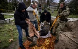 Des travailleurs communaux et un soldat ukrainien exhument le corps d'un civil, enterré près d'une église dans le village de Gostomel, dans la région de Kiev, le 12 avril 2022