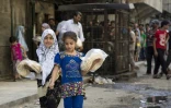 Deux jeunes filles portent des sacs de pain devant une boulangerie à Alep le 12 juillet 2016