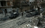 Photo prise le 25 février 2018 montrant un homme marchant dans une rue de la ville de Douma au milieu de voitures détruites et immeubles endommagés après des raids aériens du régime syrien sur la Ghouta orientale, une enclave rebelle près de Damas bombardée par le régime syrien