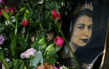 Un portrait d'Elizabeth II est vu à côté de bouquets de fleurs disposés à l'extérieur du palais de Buckingham Palace à Londres le 11 septembre 2022
