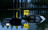 Un militant de l'ONG Greenpeace brandit une pancarte "rétrécissez maintenant ou vous coulerez bientôt", faisant allusion à la taille des automobiles et à leurs émissions de CO2, près de vieilles voitures que des militants ont partiellement immergées dans un plan d'eau proche de l'entrée du salon de l'automobile de Munich le 4 septembre 2023