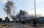 De la fumée lors d'une frappe israélienne alors que des Palestiniens marchent sur une route utilisée pour atteindre un point de distribution d'aide de la Fondation humanitaire de Gaza (GHF,) près du camp de réfugiés de Nousseirat, dans le centre de la bande de Gaza, le 25 juin 2025