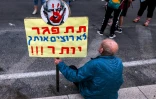 Un homme assis avec une pancarte anti-Netanyahou lors d'une manifestation à Tel Aviv
