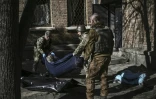Des militaires ukrainiens emmènent un cadavre dans les environs de l'Académie nationale des sciences, touchée par une frappe, à Kiev, le 22 mars 2022