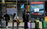 Des touristes portant des masques attendent le bus pour l'aéroport, à Barcelone (Espagne) le 15 mars 2020