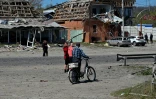 Des habitants de Merefa, dans l'est de l'Ukraine, passent près de bâtiments et de voitures endommagés par une frappe de missile russe, le 4 mai 2026
