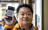 Le gouverneur de la préfecture de Yamanashi, Kotaro Nagasaki, montre un QR code en présentant les nouvelles procédures d'accès au mont Fuji, le 19 juin 2024 à Narusawa, au Japon