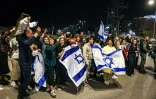 Des personnes tiennent des drapeaux israéliens et se réjouissent après le passage d'un véhicule transportant d'ex-otages israéliens vers une base militaire à Ofakim (Israël) le 26 novembre 2023
