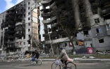 Des personnes passent à bicyclette devant des bâtiments détruits dans la ville de Borodianka le 4 avril 2022