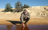 David van Wyk, chercheur principal à la Bench Marks Foundation, effectue des tests dans un cours d'eau à la décharge de la mine de Snake Park, à Soweto, le 30 mai 2025 en Afrique du Sud