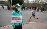 Une volontaire de l'organisation japonaise invite, via sa pancarte, le public à se tenir loin du parcours du semi-marathon de Sapporo, le 5 mai 2021