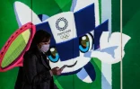 Une femme portant un masque de protection passe devant le poster de la mascotte officielle des JO 2020, le 11 mars 2020 à Tokyo