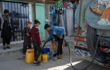 Des jeunes Afghans remplissent des bidons d'eau potable à partir d'un camion-citerne, le 27 avril 2025 à Kaboul