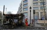 Des pompiers près d'un kiosque à journaux incendié lors de la manifestation des "gilets jaunes" sur les Champs-Elysées, le 16 mars 2019 à Paris
