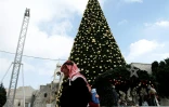 Un Palestinien le 20 décembre 2016 près d'un sapin de Noël géant place de la Mangeoire, à côté de l'Eglise de la Nativité, à Béthléem, lieu de naissance du Christ selon la Bible