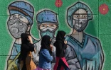 Des femmes portant un masque, devant une peinture murale à New Delhi le 19 décembre 2020