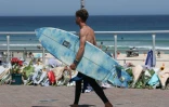 Un surfeur passe devant les fleurs déposées sur la promenade de la plage de Bondi à Sydney, le 18 décembre 2025, en hommage aux victimes de l'attentat du 14 décembre
