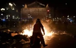 Un pompier tient une poubelle à côté d'un tas d'ordures en feu devant l'Opéra Garnier lors d'une manifestation à Paris le 20 mars 2023 ( AFP / Christophe ARCHAMBAULT )