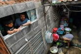 Thanapat Noidee et son fils à la fenêtre de la pièce qu'ils habitent dans un bidonville de Bangkok, le 30 mai 2020 en Thaïlande