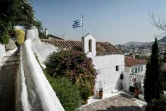 Un drapeau grec à côté de la croix d'une église à Anafiotika, un quartier situé dans la zone archéologique de l'Acropole, le 6 juillet 2018 à Athènes, en Grèce
