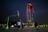Des habitants jouent au basket devant la tour illuminée de Huaxi, le 21 mai 2021 dans l'est de la Chine