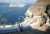 Des touristes grimpent vers le village de Fira, alors qu'un bateau de croisière arrive, sur l'île grecque de Santorin, le 20 juillet 2024