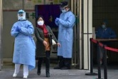 Une femme, le visage couvert d'un masque de protection contre le coronavirus, se fraie un passage entre deux membres du personnel médical à l'entrée d'un hôpital, à Shanghai le 27 février 2020