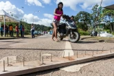 Une femme pousse son scooter devant des pointes bloquant une route vers l'aéroport le 29 mars 2017 à Cayenne, en Guyane 