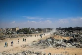 Des Palestiniens empruntent une route près d'immeubles endommagés ou détruits, le 7 avril 2024 à Khan Younès dans la bande de Gaza